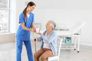 Female doctor giving senior woman suffering from Parkinson syndrome cup of tea in clinic