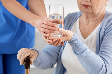 Female doctor giving senior woman suffering from Parkinson syndrome glass of water in clinic