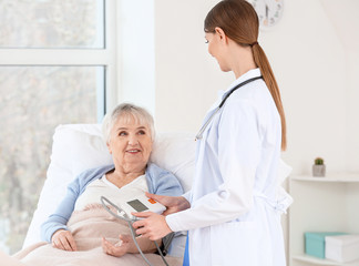 Fototapeta premium Female doctor measuring blood pressure of senior woman suffering from Parkinson syndrome in clinic
