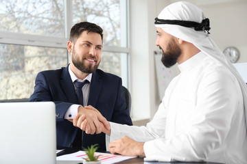 Arab man and his business partner shaking hands in office