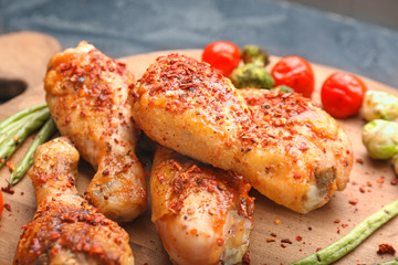 Cooked chicken drumsticks with vegetables on board, closeup