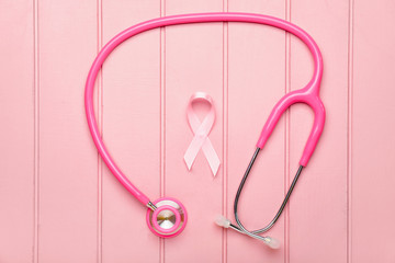 Fototapeta premium Pink ribbon with stethoscope on white wooden background. Breast cancer awareness concept