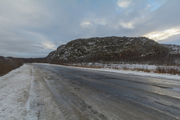 The dirt road is covered with ice .The sky is covered with clouds.