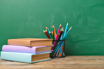 Pencils and books on table near school blackboard