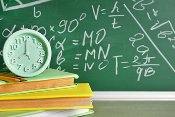 Books and clock on table near blackboard