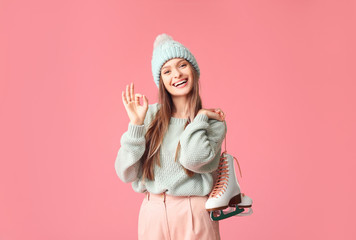 Beautiful young woman with ice skates showing OK on color background