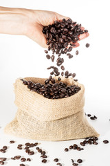 Coffee Beans falling into jute bag from female hand on white background
