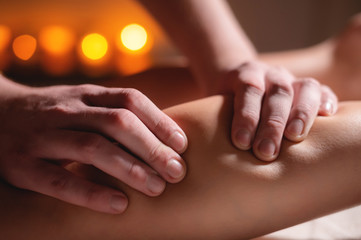 Premium male luxury shin massage anti-cellulite wellness complex. Close-up of a male masseur doing leg massage to a female client in an office with dark light on a background of burning candles