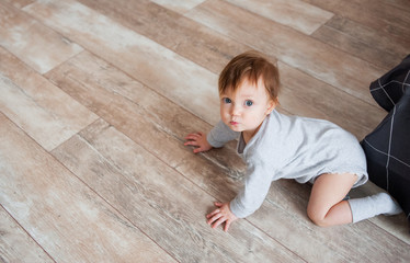 Little cute girl crawls on floor and looks at camera.
