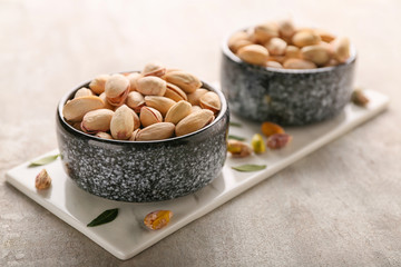 Bowls with tasty pistachio nuts on light background