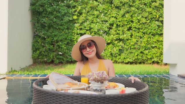 Smiling Asian brunette with shades, yellow bikini and floating breakfast