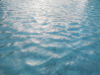 Waving pattern of vivid turquoise blue water in the swimming pool above stone tiles with soft light of reflection of the sunshine