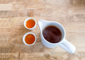 A jar of hot tea and two cups on brown wooden table for drinking time, top view image