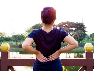 adult thai asian woman with exercise and stretching body in park from backache and waist pain.
