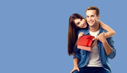 Love, relationship, dating, flirting, lovers concept - happy smiling amorous couple opening gift box. Blue color background. Copy space for some text.