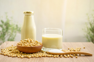 Fresh soybean seeds in brown wooden bowl, sugar in a spoon and two bottles of soy milk on the table,  under sunlight morning blurred background, delicious healthy drinking for breakfast