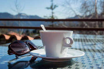 A cup of coffee outdoors, sunglasses, close-up of a hot beverage and mountain in the background
