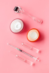 Dermatologist work desk with tools. Dermaroller, syringe, ampoule on pink background top-down flat lay