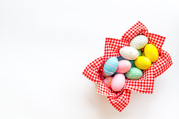 Easter eggs painted in basket on white desk top-down copy space