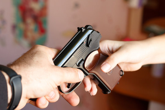 Adult man hands a gun to a child