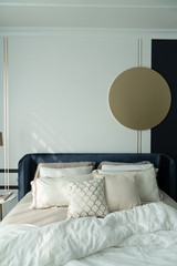 Bedroom corner navy blue velvet bed with soft pillows setting decorated with circular marble night table and navy blue paint wall in the background / cozy interior design