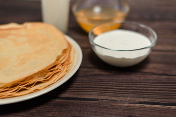 Maslenitsa is a holiday at the end of February . pancakes with sour cream, honey and milk on a dark wooden background. close up. blini. space for text.