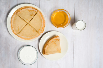 Maslenitsa is a holiday at the end of February . pancakes with honey, sour cream and milk on a light wooden background. honey trickles down a stack of pancakes. close up. blini. space for text.