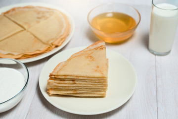 Maslenitsa is a holiday at the end of February . pancakes with honey, sour cream and milk on a light wooden background. honey trickles down a stack of pancakes. close up. blini. space for text.
