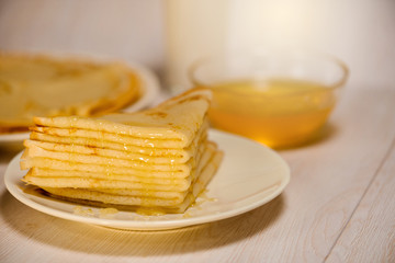 Maslenitsa is a holiday at the end of February . pancakes with honey and milk on a light wooden background. honey trickles down a stack of pancakes. close up. blini. space for text