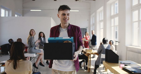 Happy young Caucasian male office employee walks into new multiethnic office hired on a new job, colleagues welcome him.