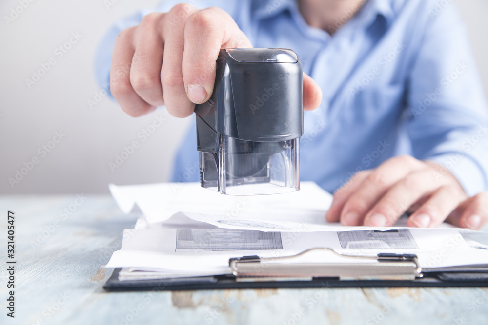 Poster Businessman puts a stamp on the documents in the office.