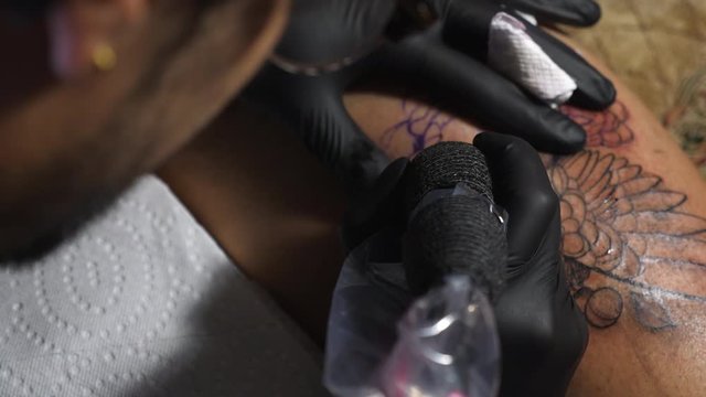 A Tattoo Artist With Gloves Slowly Tracing Art Design Into The Skin Of A Customer Using Tattoo Machine In Vancouver Tattoo Shop - Close Up Shot 