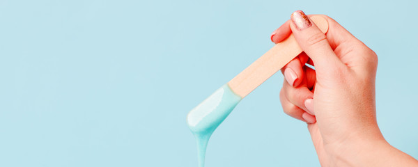 depilation and beauty concept - sugar paste or wax honey for hair removing with wooden waxing spatula sticks in hand on blue background, copy space, beauty industry, concept of smooth skin remove - 321407249