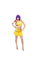 a girl in yellow clothes and a blue wig stands playfully and smiles on a white background with a candy Lollipop