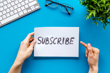 Subscribe. Advertisement in hand on blue office desk top-down