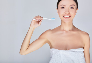 A young Asian woman in a white towel after a shower brushes her teeth.