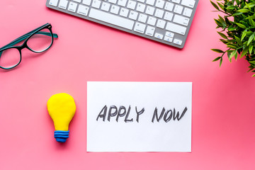 Apply now. Text on pink office desk top-down