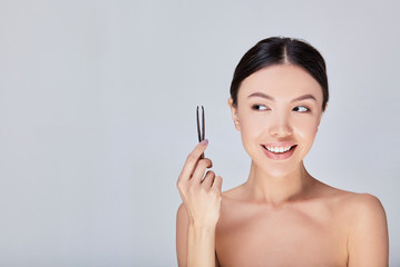 A cute Asian woman holds tweezers in her hands.
