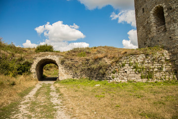 Fototapeta na wymiar castle wall fortress construction building stone wall arch shape passage ground dirt trail and vivid blue sky background clear weather day time