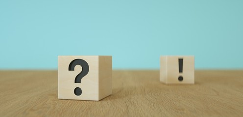 wooden cubes with black question mark  foreground and exclamation mark sign in the background on wooden table
