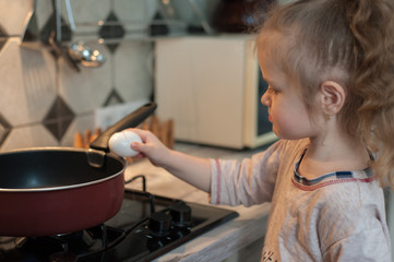 Little girl cooks fried eggs in a pan