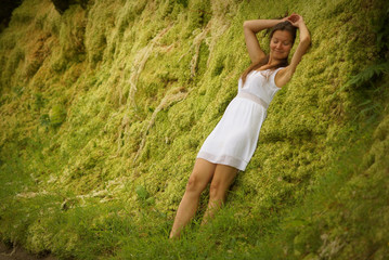 Beutiful young girl leaning against green moss wall near road. Expression of relaxation and...