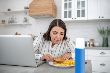 Dark-haired woman in a striped blouse looking at the plate with food