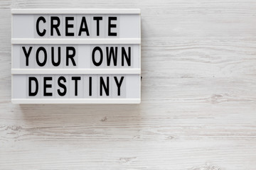 'Create your own destiny' words on a modern board on a white wooden background, top view. Overhead,...