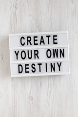 'Create your own destiny' words on a lightbox on a white wooden background, top view. Overhead, from above, flat lay. Close-up.