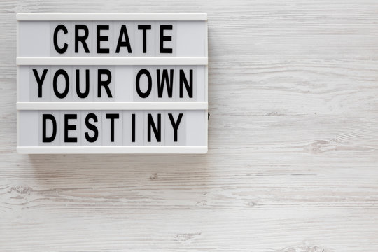 'Create your own destiny' words on a modern board on a white wooden background, top view. Overhead, from above, flat lay. Space for text.