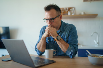 Thoughtful serious young man lost in thoughts in front of laptop, focused businessman thinking of problem solution, worried puzzled man looking ar laptop screen