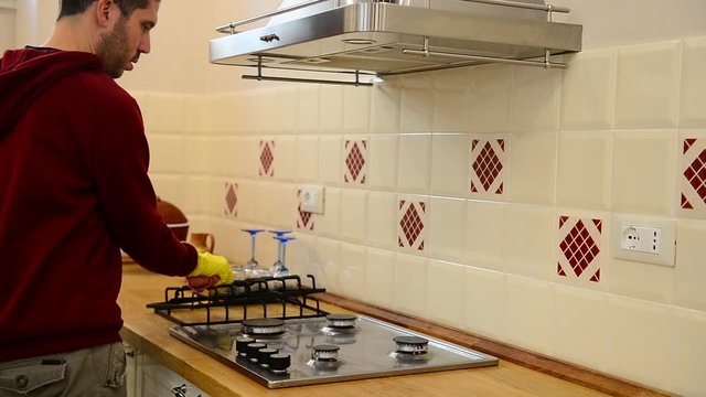 Caucasian man cleaning cookers with spray, spoonge and gloves