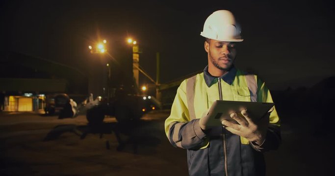 African foreman managing gravel stone loading on digital tablet working night shift