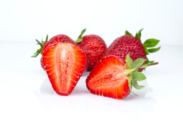 Red strawberries cut in half, on a white isolated background with a mirror glossy reflection on the table surface